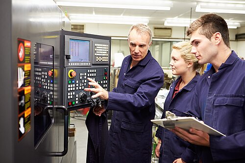 A man showing two apprentices how to use a machine.