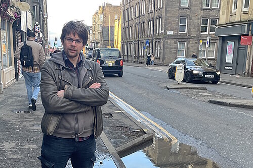 Councillor Jack Caldwell standing on a pavement on Easter Road with cars behind him