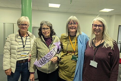 WASPI campaigners, one of whom is Councillor Chris Brett, posing for an indoor photo. One wears a sash with the word "WASPI" on it. They all look as if they mean business.