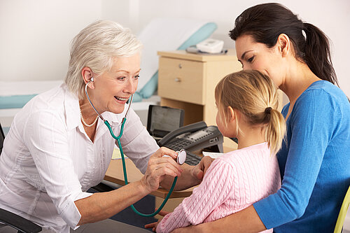 A mother holding a child whilst a GP checks on her using a stethoscope.