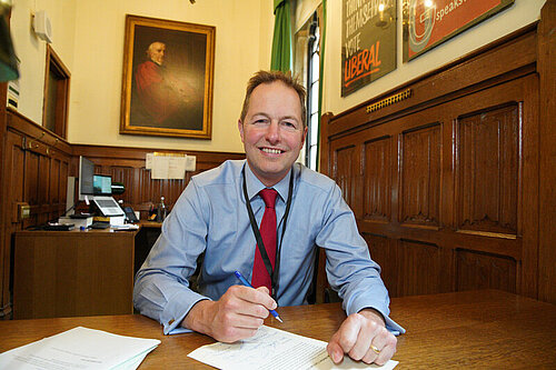 Richard Foord sitting at a desk in Parliament with a pen and note-paper