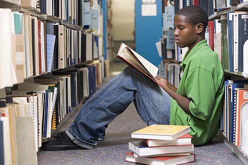 A child sitting on the floor in a library reading a book.