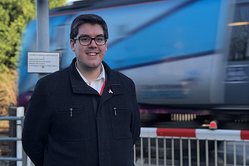 Ed Pearson standing by a level crossing as a train passes behind