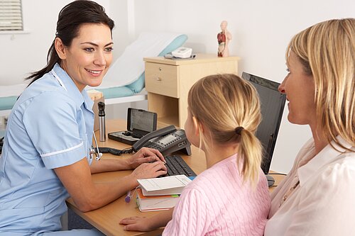 A nurse tending to a child patient, who is sitting on her mothers lap.