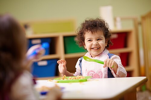 A toddler eating food off a plate with a spoon.